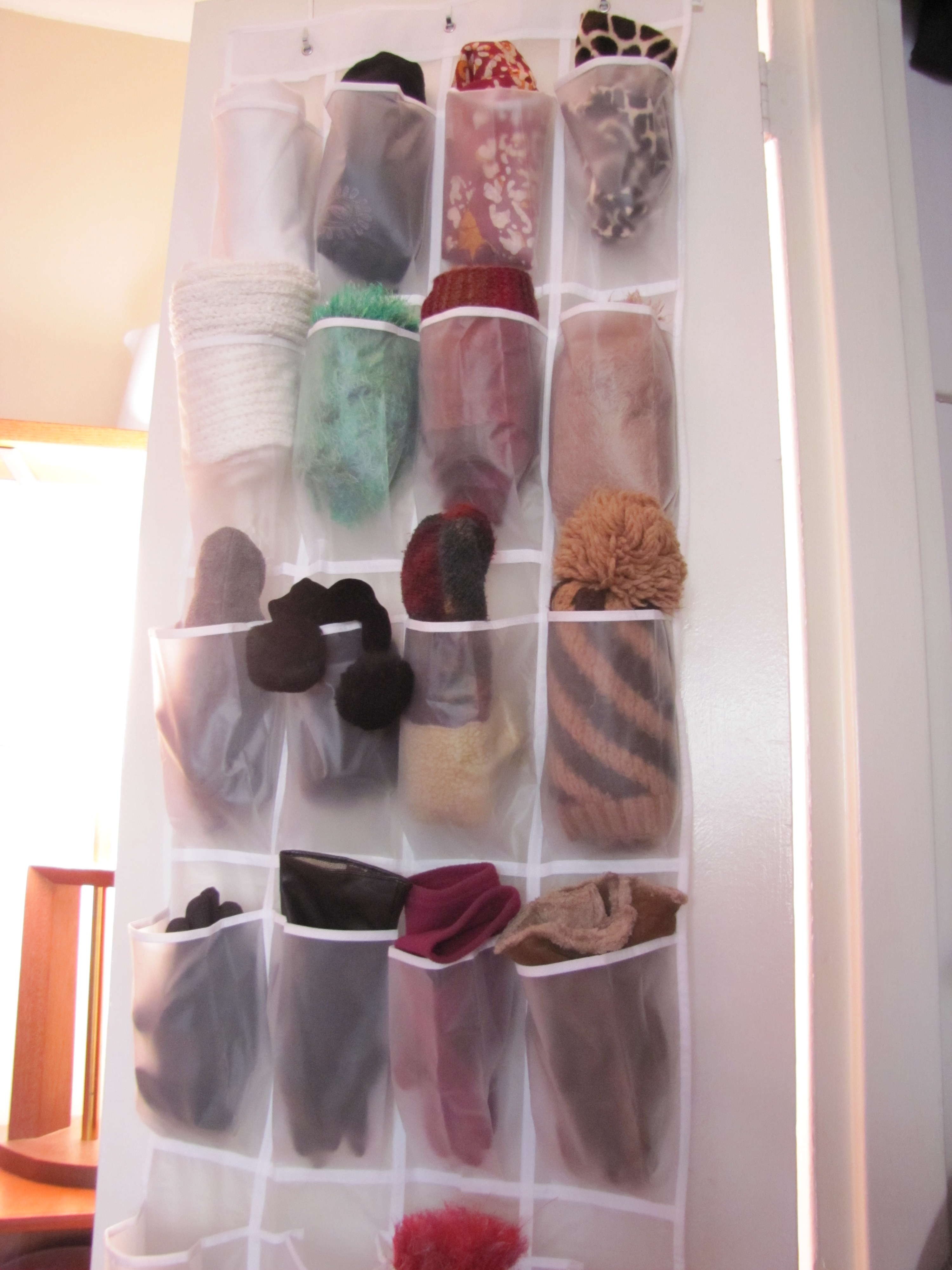 A shoe organizer storing winter gloves, scarves, and hats on a door.